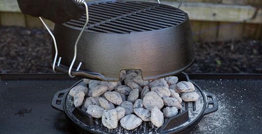 A person uses the hook and carry handles to place to the grill grate dome top onto the base of the Kickoff Grill